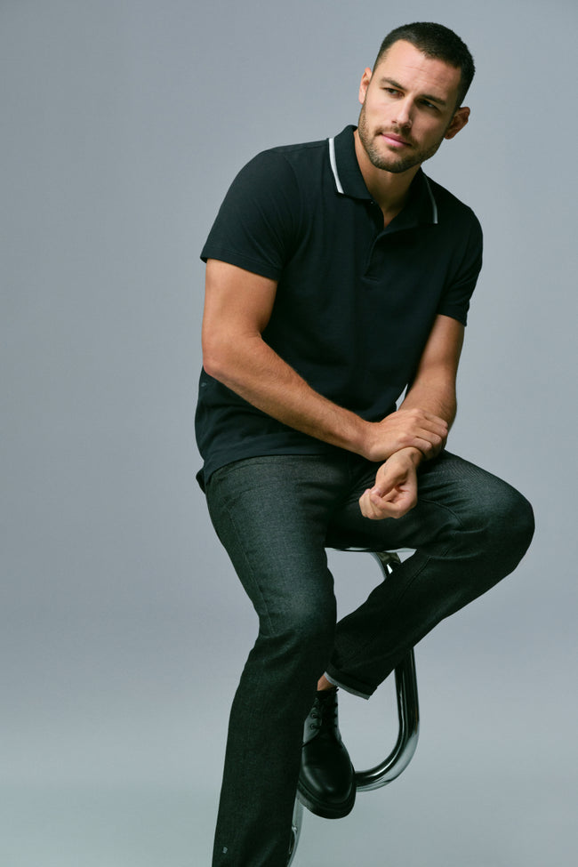 Man sits on a stool wearing SILVER polo and SILVER Denim