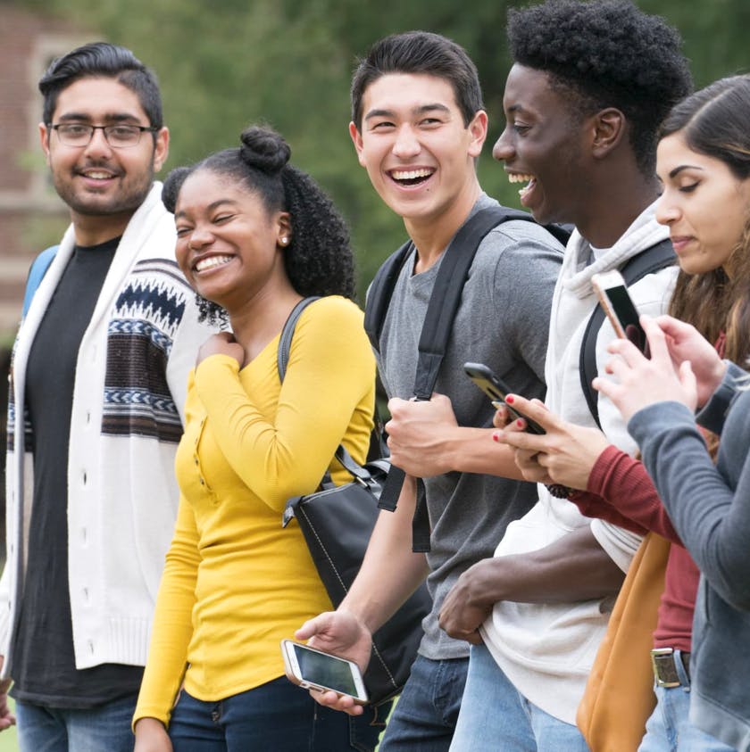 5 young adults laughing and walking with their backpacks and phones