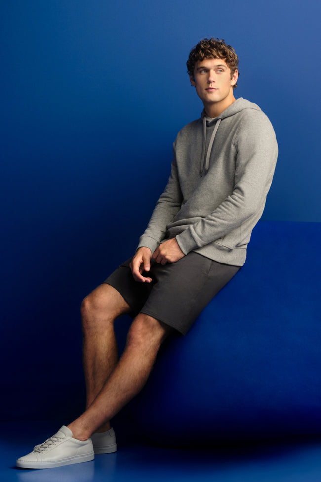 Man leans up against blue blob. The man is wearing a grey hoodie and grey sweatshorts