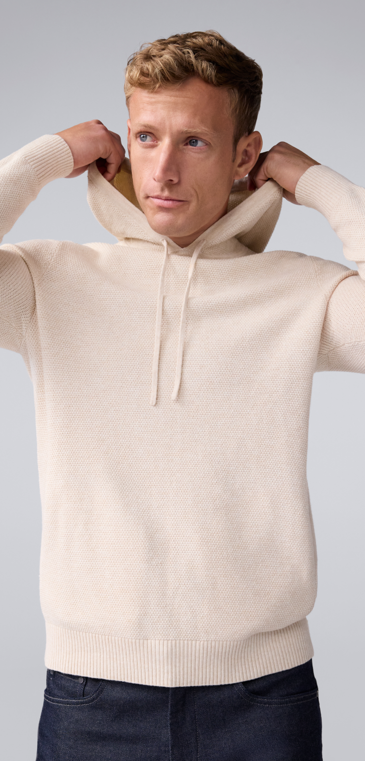 Image of a man putting on the hood of his cream Tech Linen hoodie